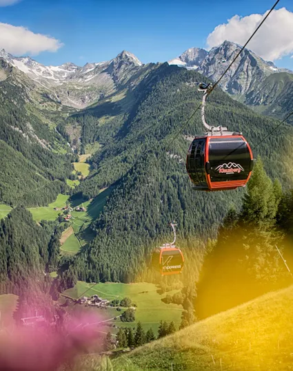 Rote Gondeln des K-Express Klausberg fahren über grünes Ahrntal mit Blick auf Bergpanorama