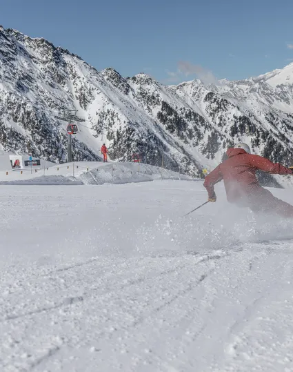 Skifahrer in roter Kleidung carvt auf präparierter Piste am Klausberg mit Ahrntaler Bergpanorama