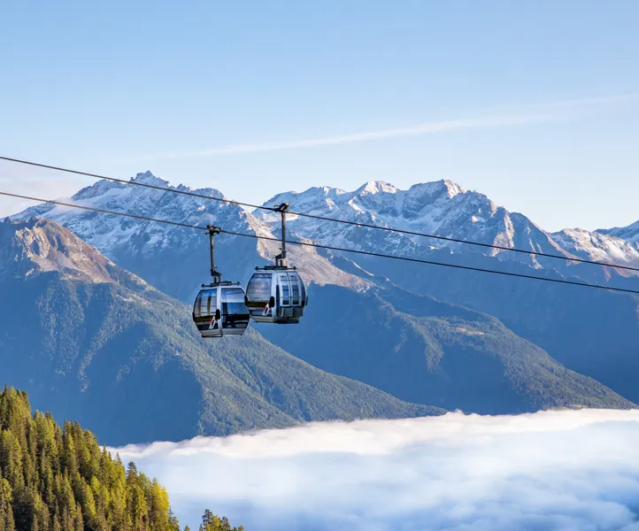 Seilbahnkabinen über dem Nebelmeer im Ahrntal mit schneebedeckten Tauern-Gipfeln im Herbst