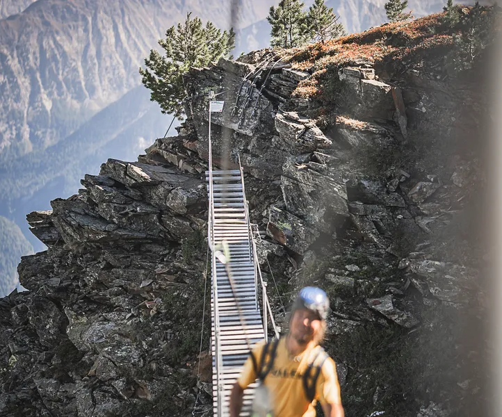 Klettersteiggeher auf schmaler Holzlatten-Hängebrücke über Felsgrat, Bergpanorama Südtirol