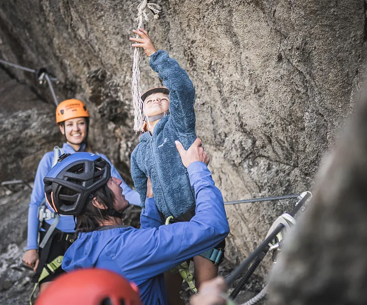 Familie am Klettersteig Ahrntal: Kind läutet Gipfelglocke, Eltern mit Helmen freuen sich