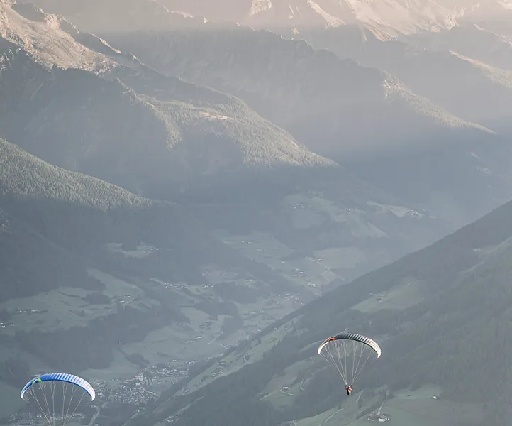 Zwei Paragleiter mit bunten Schirmen in der Abendsonne über dem grünen Ahrntal, Südtirol