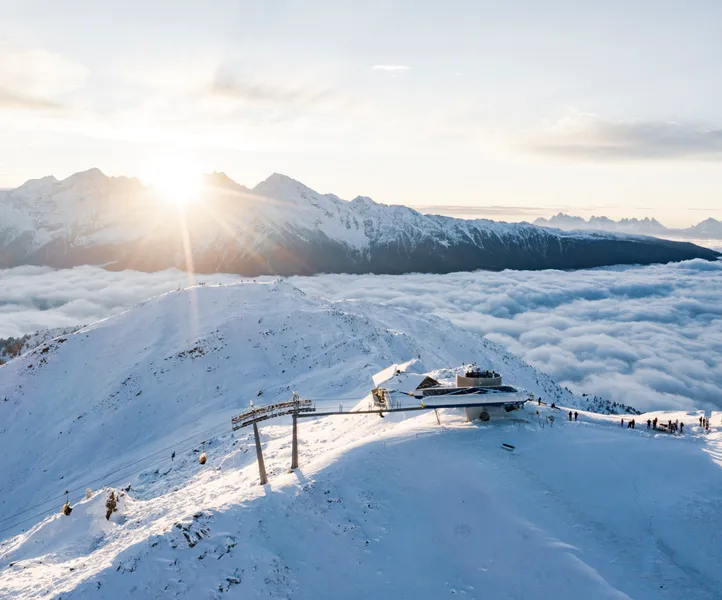 Luftaufnahme der Bergstation Sonnklar bei goldenem Sonnenaufgang über dem Wolkenmeer