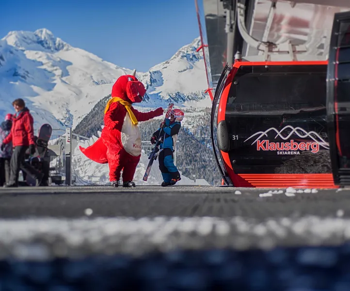 Maskottchen Drache begrüßt Kind an der Klausberg-Bergstation mit Bergpanorama