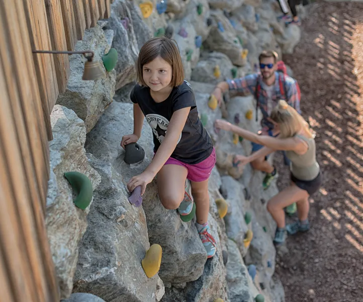 Mädchen klettert konzentriert an großer Outdoor-Kletterwand mit bunten Griffen im Sommer im Ahrntal
