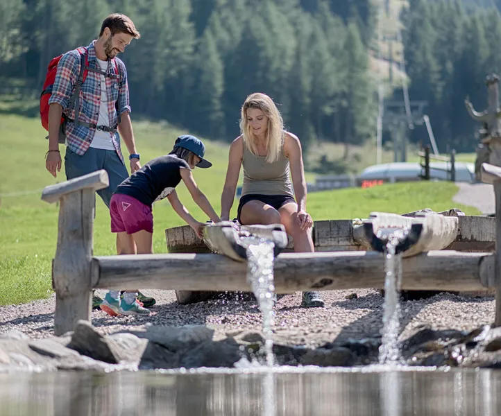 Familie erkundet Wasser-Erlebniswelt am Klausberg mit hölzernen Wasserrinnen im Sommer im Ahrntal