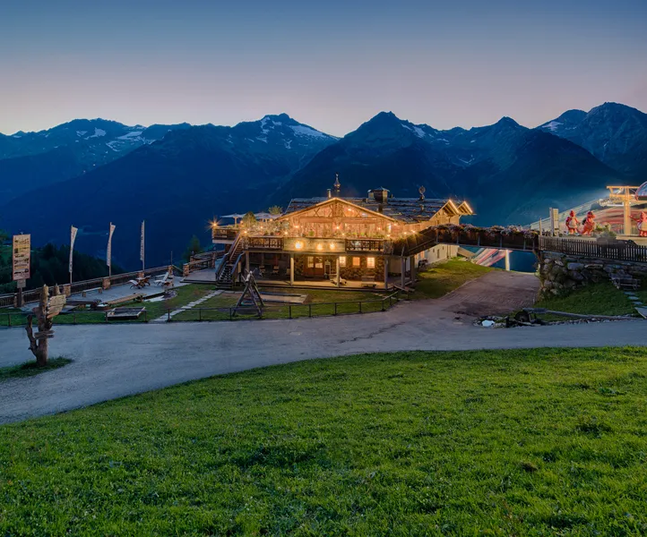 Beleuchtete Almhütte bei Sonnenuntergang mit Panoramablick auf die Zillertaler Alpen am Klausberg