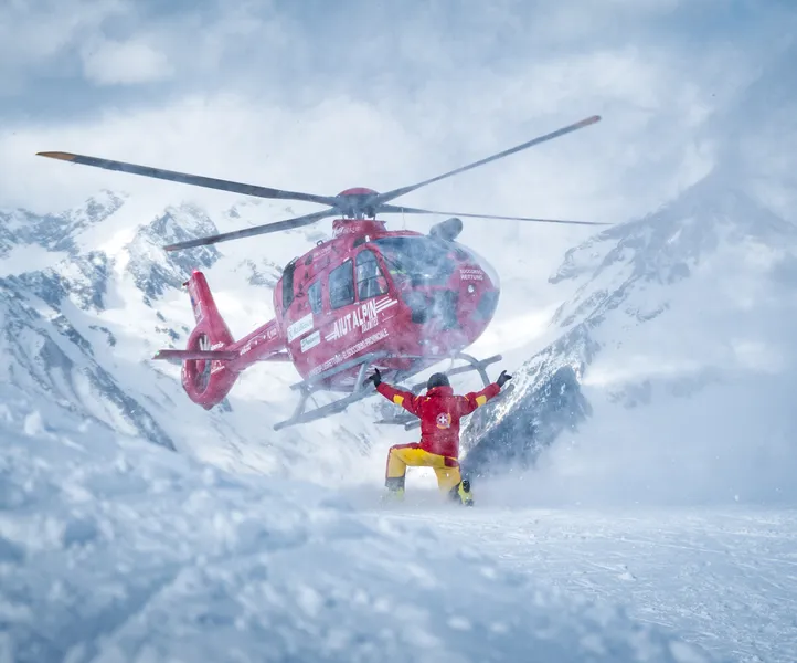 Roter Rettungshubschrauber Aiut Alpin Dolomites landet im Tiefschnee bei Pistenrettung