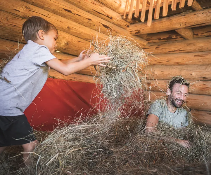 Vater und Sohn haben Spaß beim Spielen im Heu in einer Almhütte