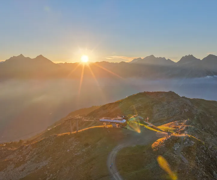 Sonnenaufgang an der K1-Bergstation Klausberg mit Nebelmeer im Tal und Paraglider