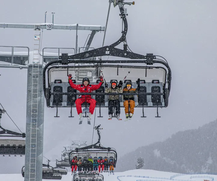 Skifahrer auf Sessellift am Speikboden bei Schneefall mit jubelndem Skilehrer in roter Uniform
