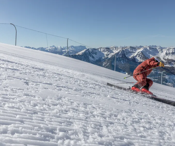 Skifahrer im roten Anzug beim Carving auf perfekt präparierter Piste am Klausberg