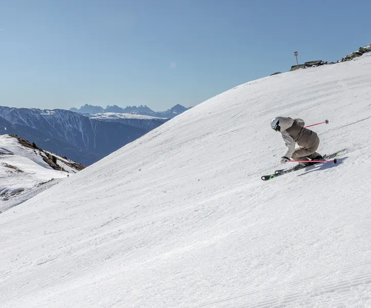 Skier in dynamic carving position on wide slope with Dolomites panorama
