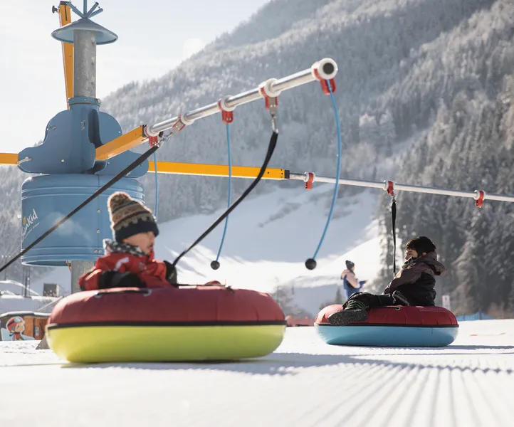 Kinder auf bunten Snowtubes am Snow-Tubing-Karussell im Kinderland des Ahrntals