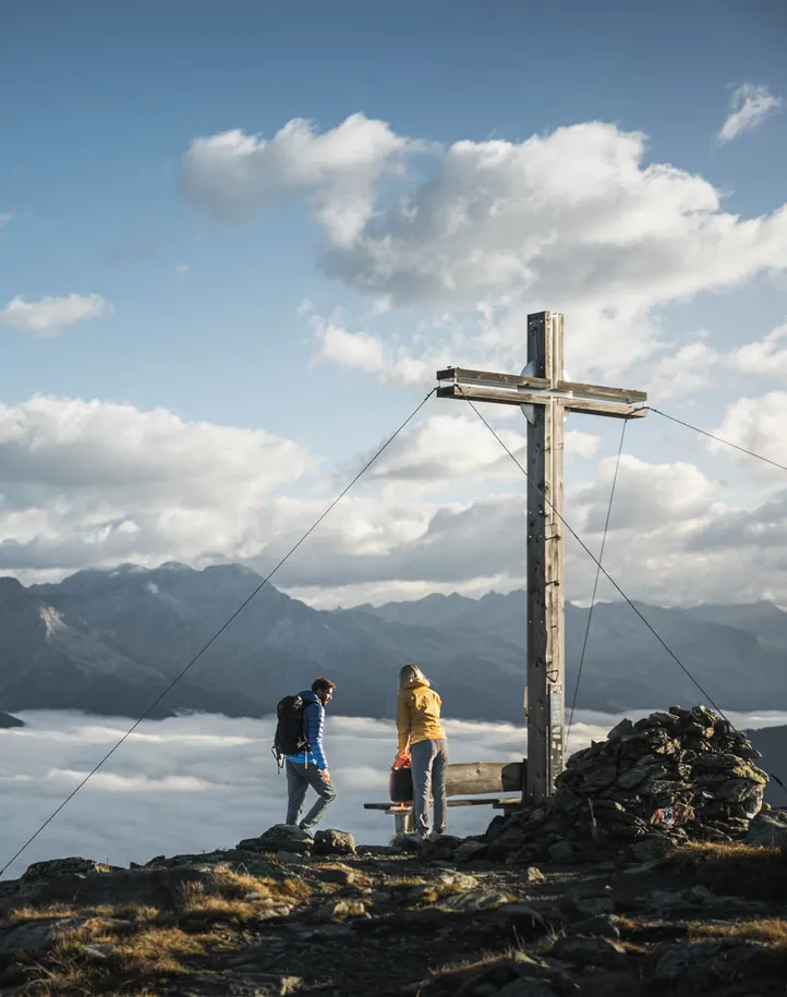 Wanderpaar am Gipfelkreuz über dem Wolkenmeer mit Panoramablick auf die Südtiroler Alpen im Ahrntal