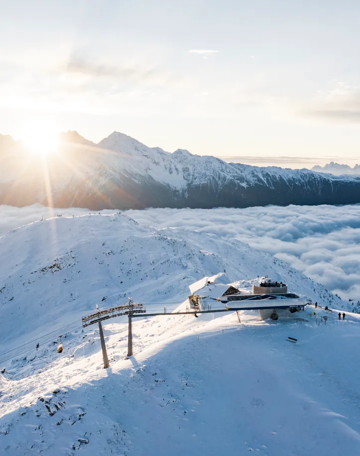 Luftaufnahme der Bergstation Sonnklar bei goldenem Sonnenaufgang über dem Wolkenmeer