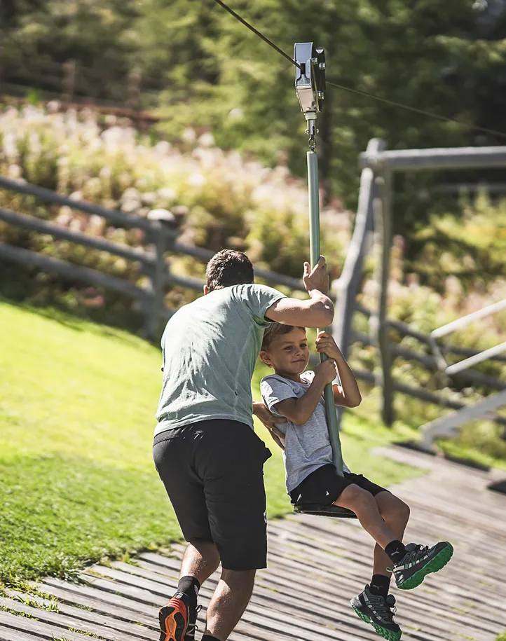 Kind auf Seilrutsche am Bergspielplatz Klausberg, Vater hilft beim Anstoßen