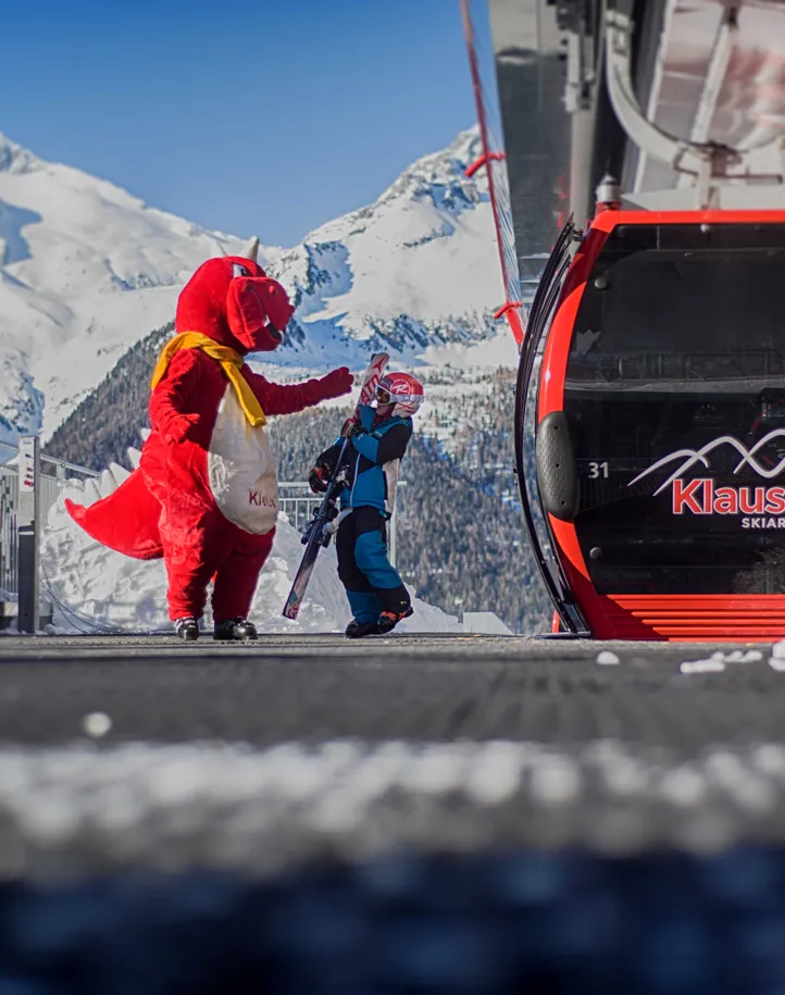 Maskottchen Drache begrüßt Kind an der Klausberg-Bergstation mit Bergpanorama