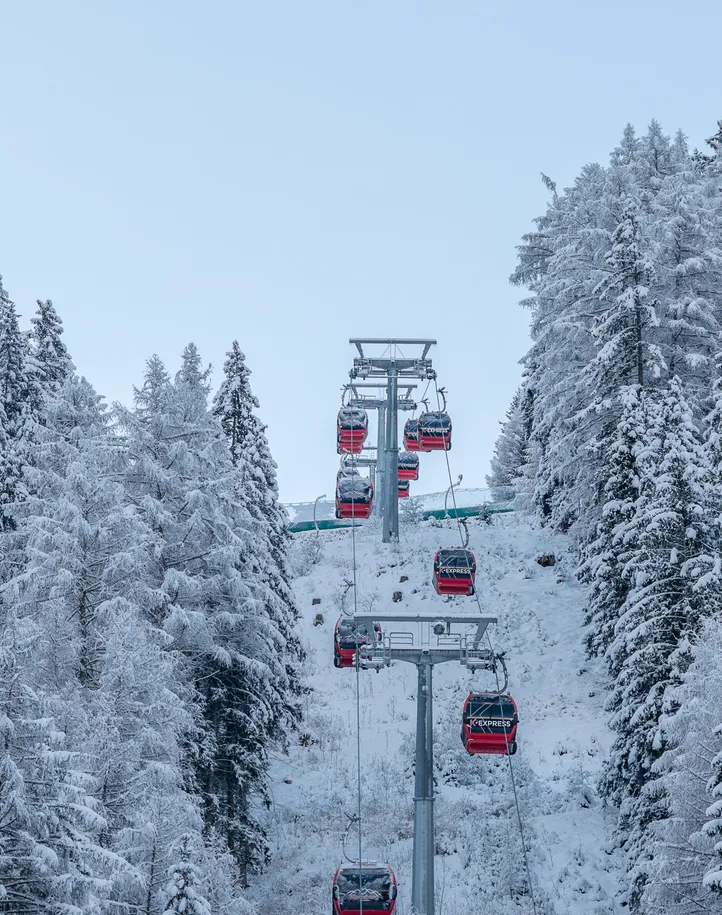 K-Express gondola lift at Klausberg ascending between snow-covered fir trees in winter