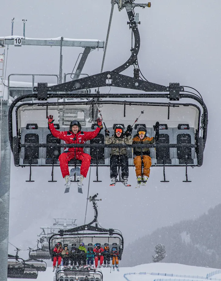 Skifahrer auf Sessellift am Speikboden bei Schneefall mit jubelndem Skilehrer in roter Uniform