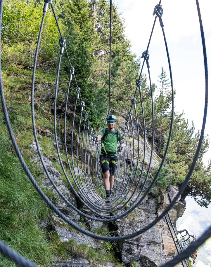 Kletterer überquert Drahtseil-Hängebrücke mit Stahlringen im Zirbenwald, Klettersteig Ahrntal
