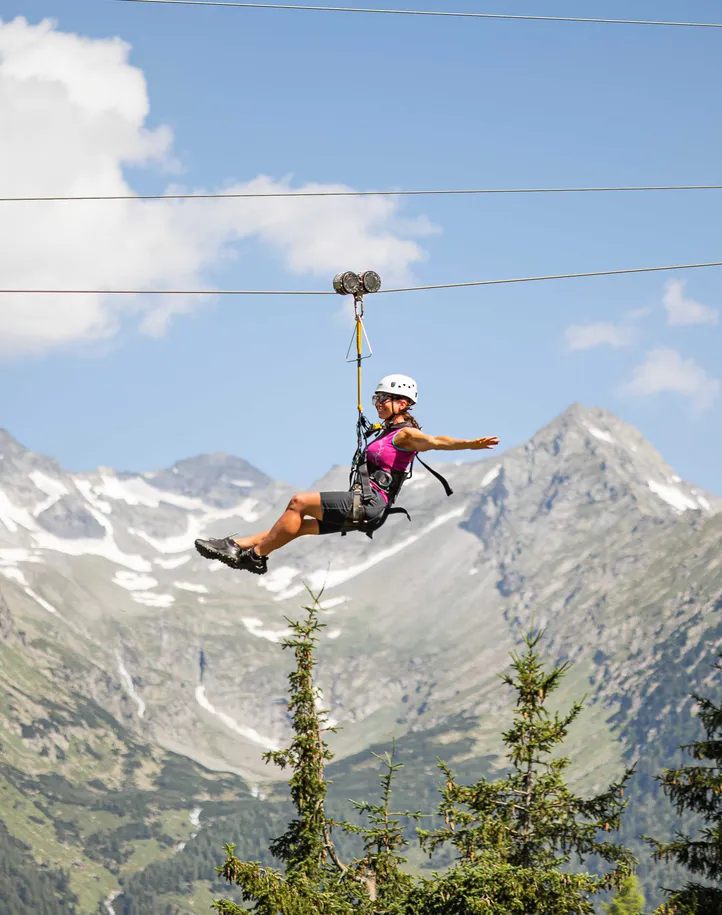 Frau im Freiflug am Skyglider Klausberg über Lärchenwäldern mit Bergpanorama Ahrntal