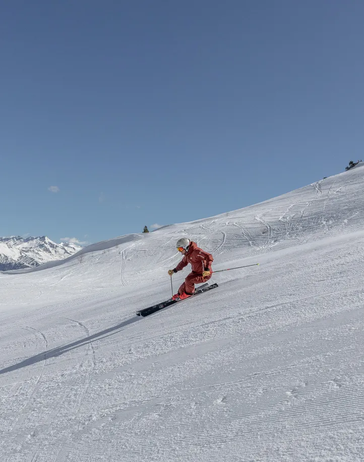 Skifahrerin in roter Kleidung auf frisch präparierter Piste am Klausberg mit Bergpanorama