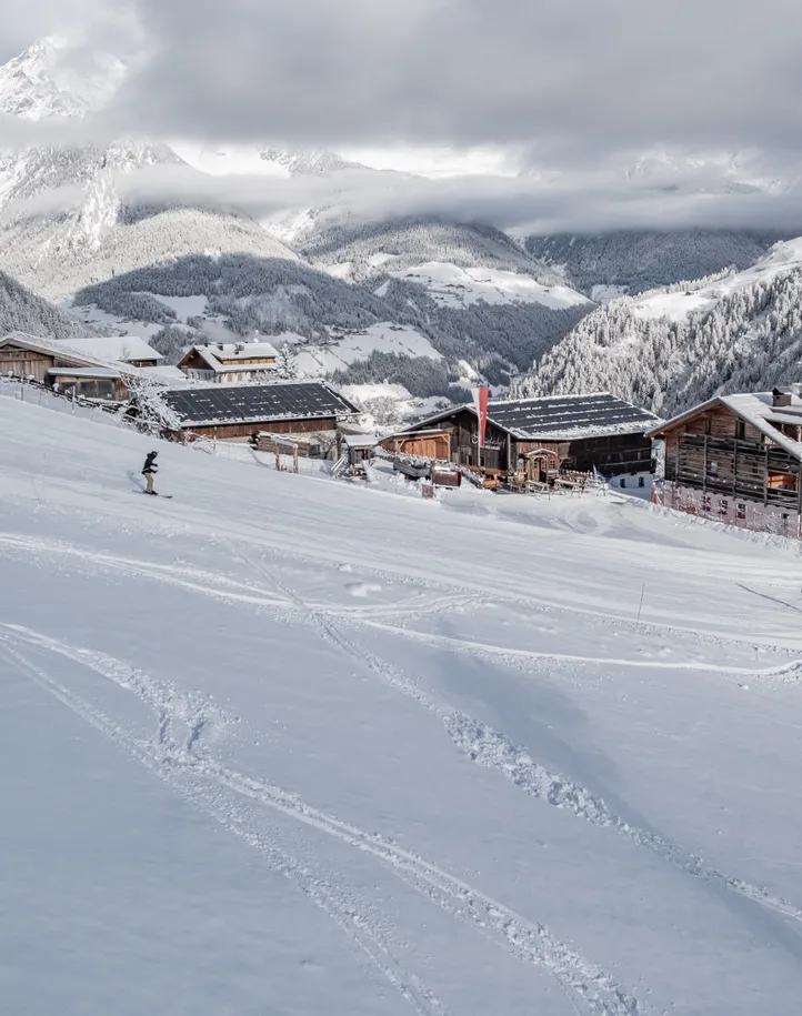 Snowboarder und Skifahrer auf Klausberg-Piste mit Almhütten und verschneitem Ahrntal Panorama
