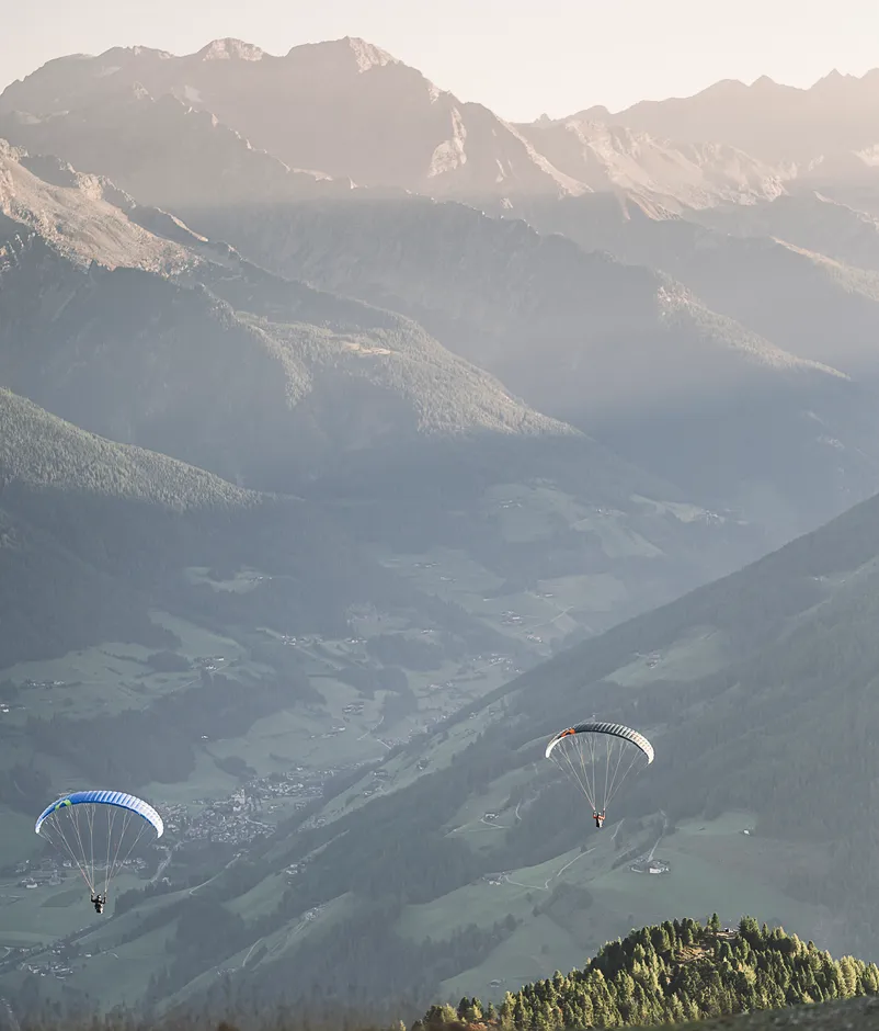 Zwei Paragleiter mit bunten Schirmen in der Abendsonne über dem grünen Ahrntal, Südtirol