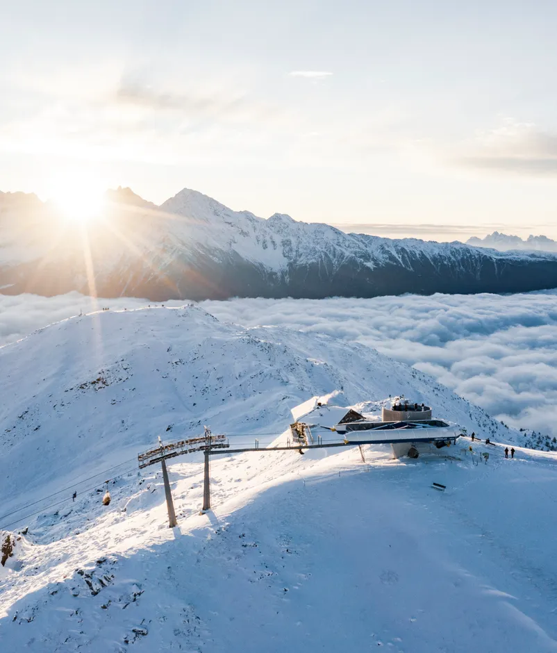 Luftaufnahme der Bergstation Sonnklar bei goldenem Sonnenaufgang über dem Wolkenmeer