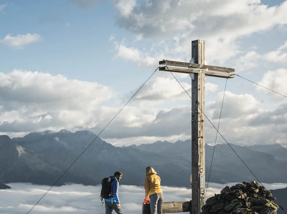 Wanderpaar am Gipfelkreuz über dem Wolkenmeer mit Panoramablick auf die Südtiroler Alpen im Ahrntal