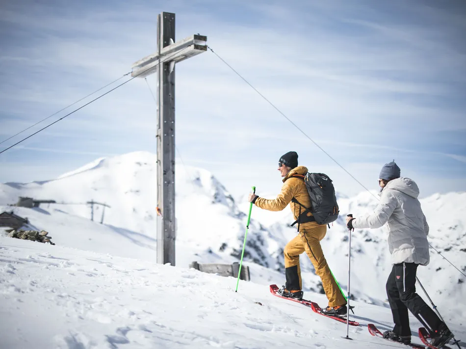 Schneeschuhwanderer beim Aufstieg zum Gipfelkreuz am Speikboden mit winterlichem Alpenpanorama