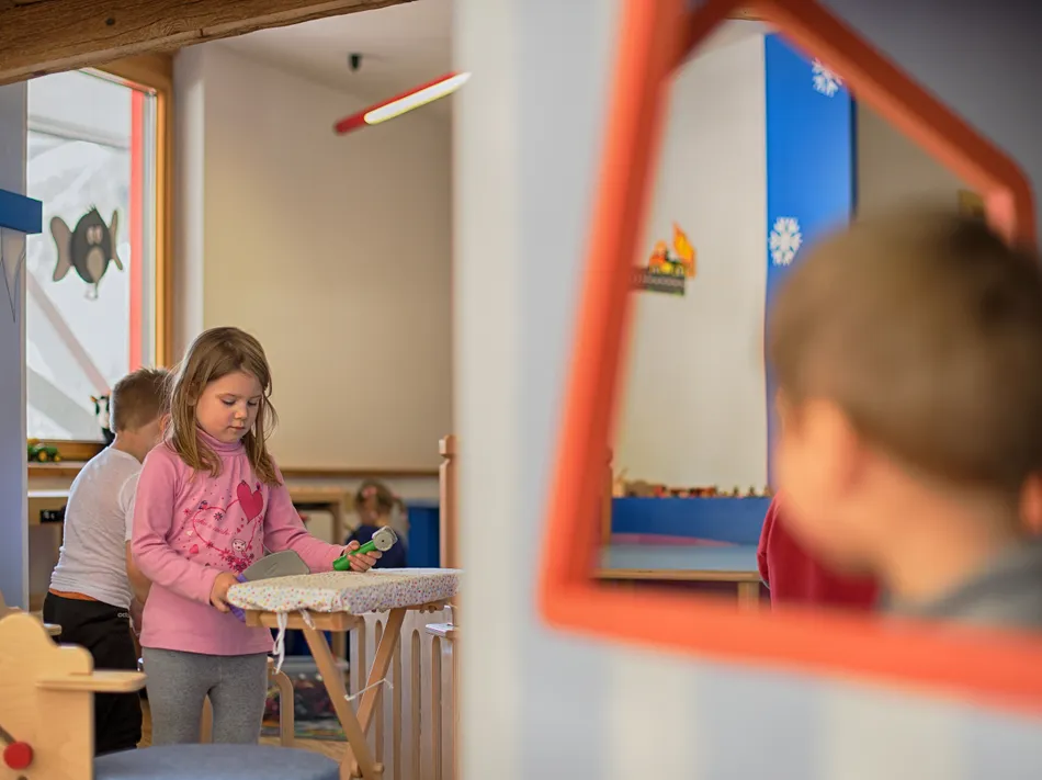 Kind spielt im warmen Skikindergarten mit Holzspielzeug in familienfreundlicher Bergstation