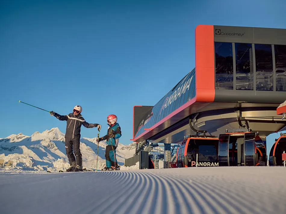Ski instructor with child on groomed slope in front of the modern gondola lift at Klausberg Ahrntal