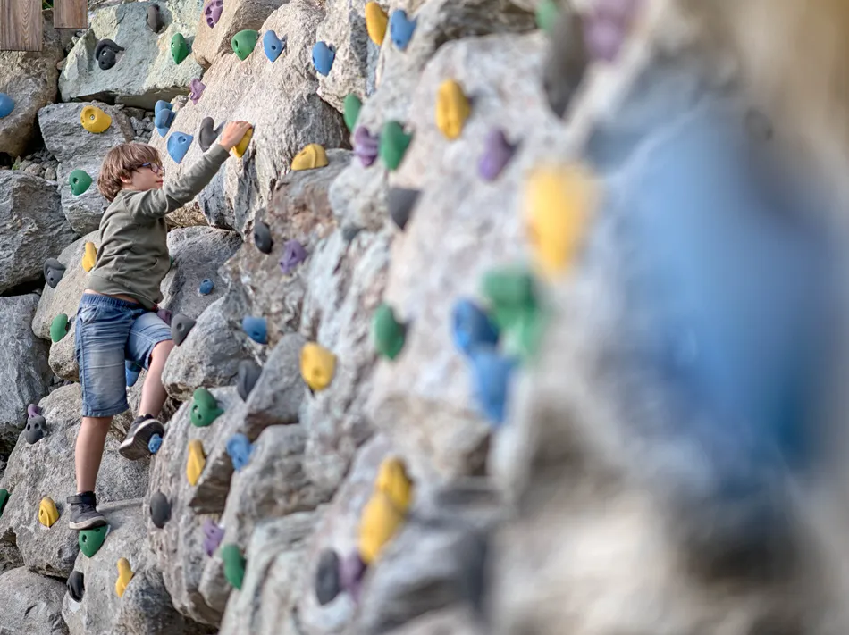 Junge mit Brille bouldert an großer Outdoor-Kletterwand mit bunten Griffen – Sommererlebnis am Klausberg