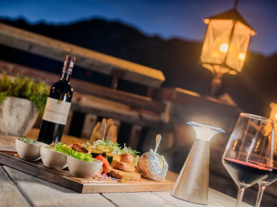 Südtiroler Hüttengericht mit Rotwein auf der Almhüttenterrasse am Klausberg bei Dämmerung
