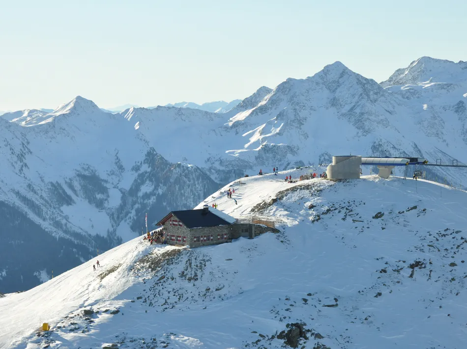 Mountain top at Klausberg with rustic stone restaurant, summit station and skiers in Alpine panorama