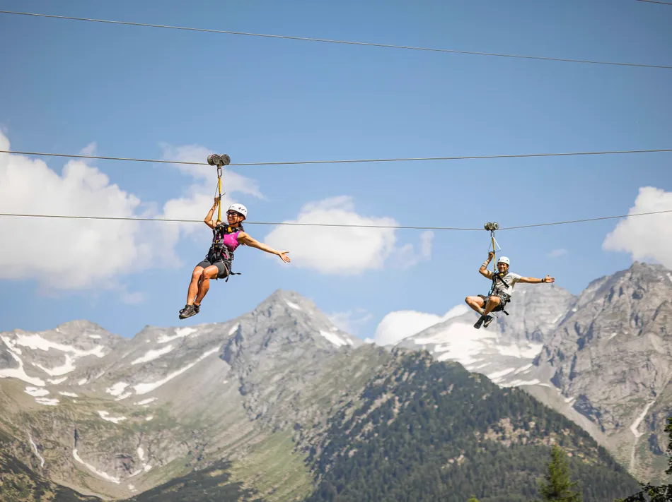 Zwei Personen sausen auf parallelen Ziplines durch die Luft, Zillertaler Alpen im Hintergrund