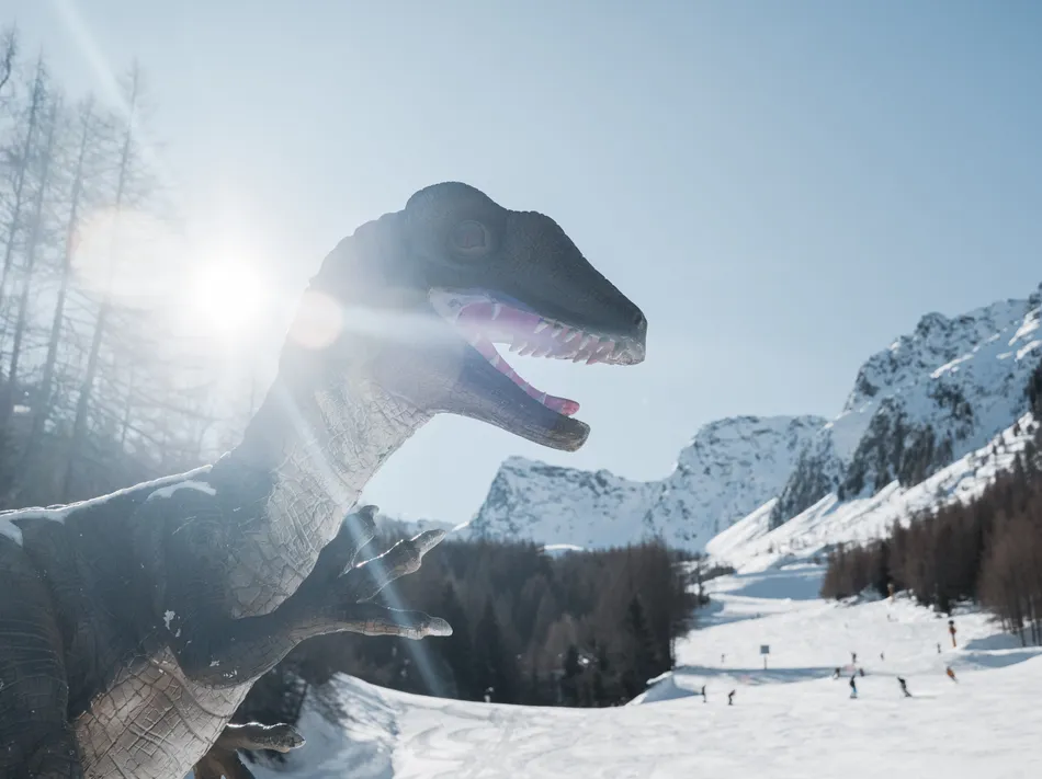 Dinosaur figure in the Dino-Park at Klausberg in front of ski slope and snowy mountain scenery