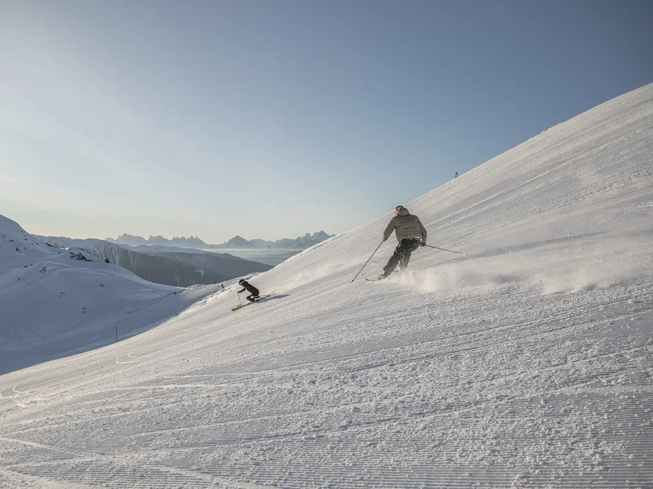 Two skiers carving in golden morning light on an empty slope with Dolomites peaks
