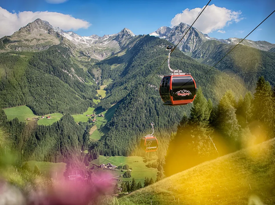 Rote Gondeln des K-Express Klausberg fahren über grünes Ahrntal mit Blick auf Bergpanorama