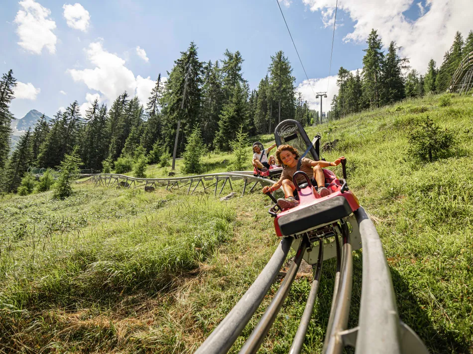 Skiworld Ahrntal Klausberg-Flitzer Alpine Coaster mit Kind und Vater auf grüner Almwiese