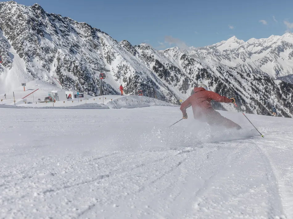 Skifahrer in roter Kleidung carvt auf präparierter Piste am Klausberg mit Ahrntaler Bergpanorama