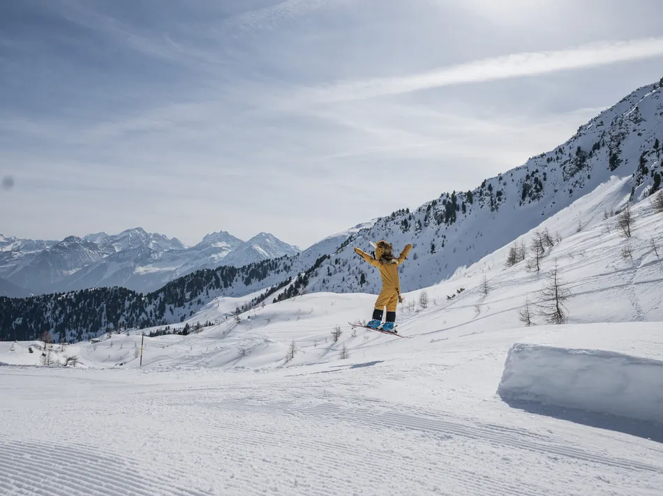 The ski resort mascot in yellow costume jumps on skis over a kicker in Ahrntal